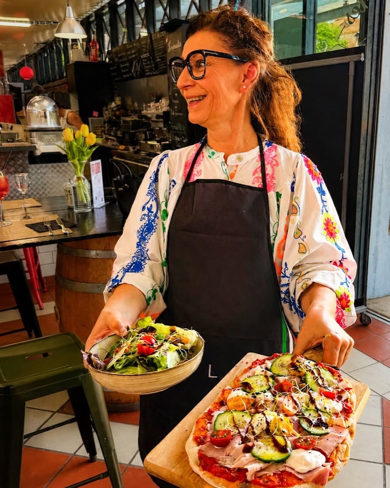La gérante de Casa Italia présentant une pizza garnie et une salade fraîche
